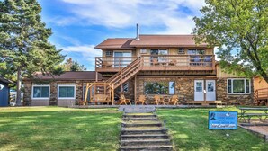 A two-story wooden building with a stone facade, a staircase leading to a balcony, and outdoor seating.