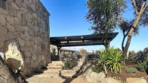 A stone building with a wooden pergola, a stone staircase, and a fenced area with plants. - Exceptional sheepfold with heated pool, close to amenities (Sotta)