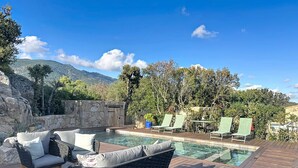 A pool area with lounge chairs, a wooden deck, and a stone wall. - Exceptional sheepfold with heated pool, close to amenities (Sotta)