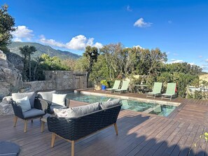 Ein Poolbereich mit Liegestühlen, einer Holzterrasse und einer Steinmauer.