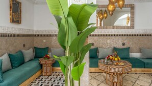 Ein marokkanisch eingerichtetes Wohnzimmer mit einer Couch, Zierkissen, einer großen Pflanze, einem Couchtisch mit Muster und verzierten Leuchten.