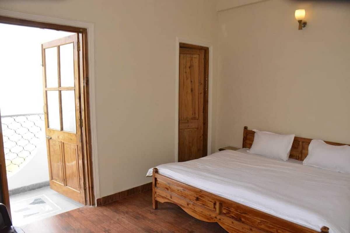 A bedroom with a wooden bed, a wooden door, and a small wall-mounted light fixture.