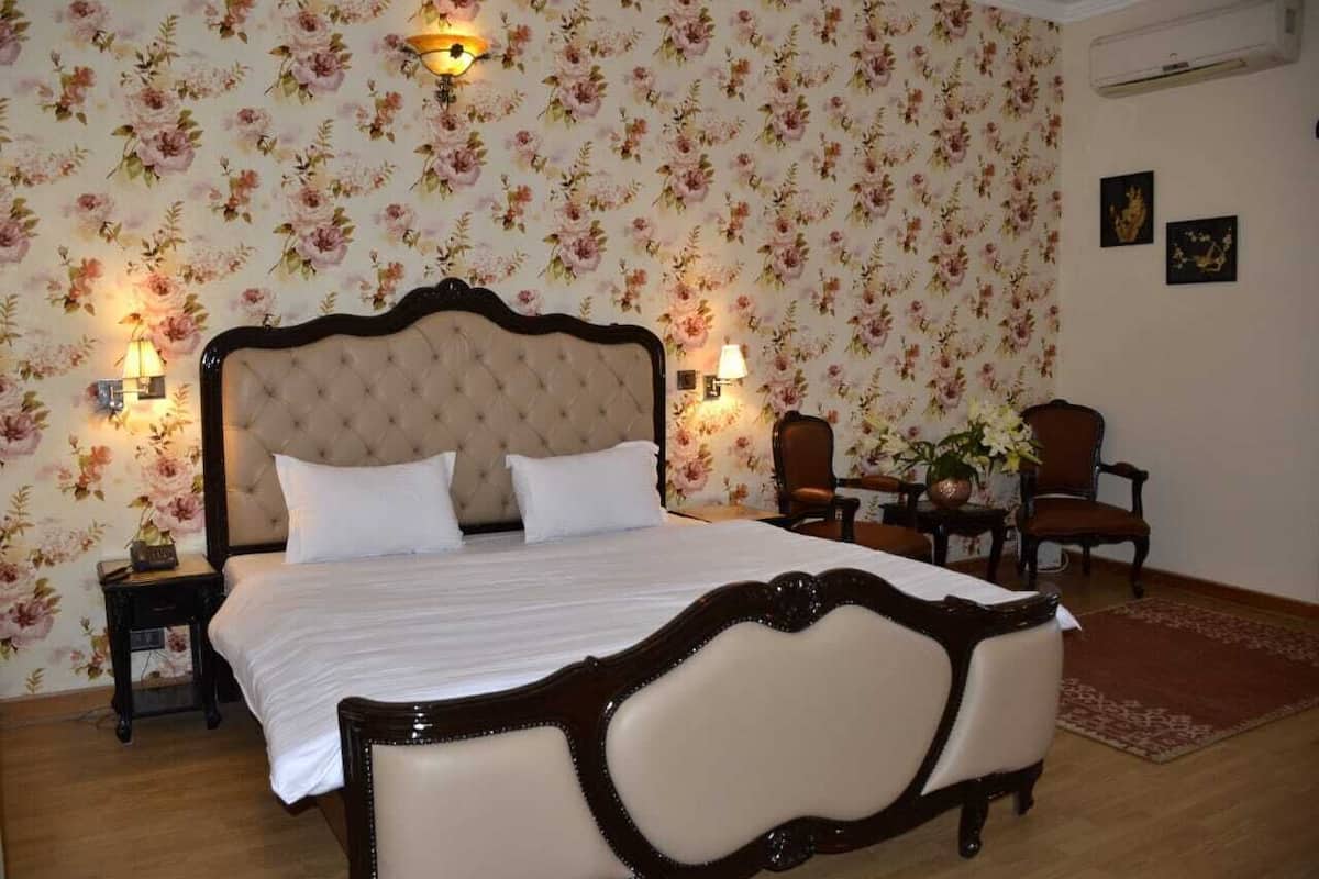 A bedroom with a large bed, two bedside tables, a chair, and floral wallpaper.