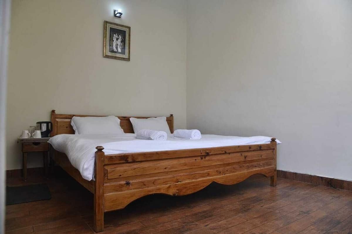 A wooden bed in a room with a nightstand, a framed picture on the wall, and a wooden floor.
