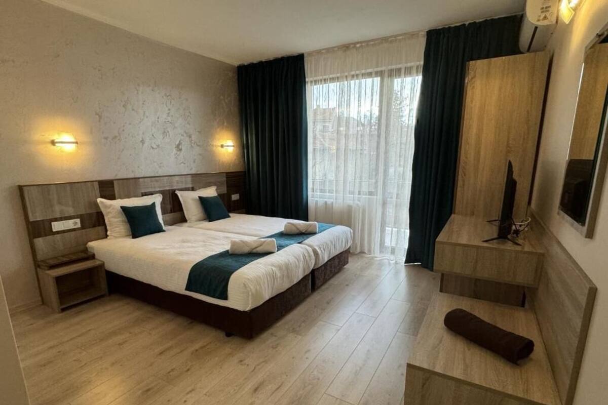 A hotel room with a large bed, bedside tables, a TV, and a window with curtains.