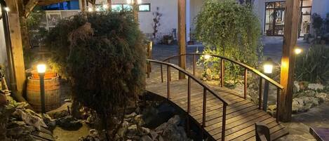 Un puente de madera sobre terreno rocoso, con un árbol y un barril.