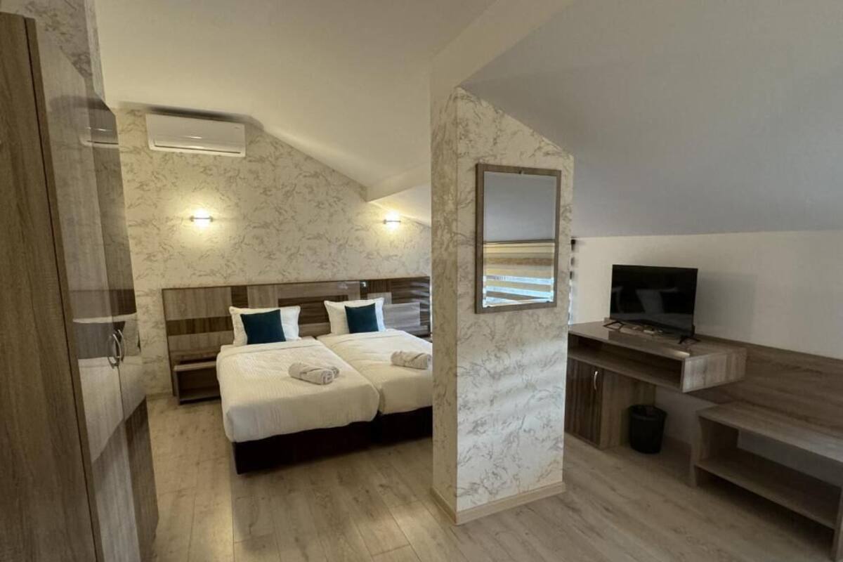 A bedroom with a bed, bedside tables, a TV, and a bathroom with a shower and toilet.