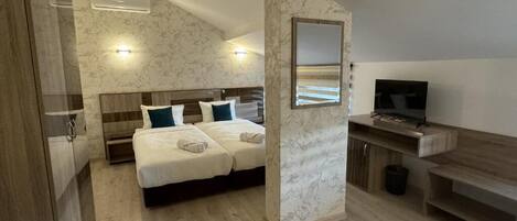 Un dormitorio con cama, mesitas de noche, televisor y baño con ducha e inodoro.