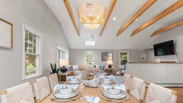 Un espace repas avec une longue table dressée pour le repas, des poutres en bois au plafond et un téléviseur en arrière-plan.