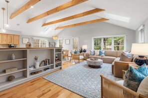 A spacious living room with wooden beams, a large window, a sofa, a coffee table, and a bookshelf. - Game Room, Central AC, Dog Friendly! (Orleans)