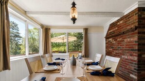 Un coin repas avec un mur en briques, de grandes fenêtres et une table dressée pour quatre personnes.