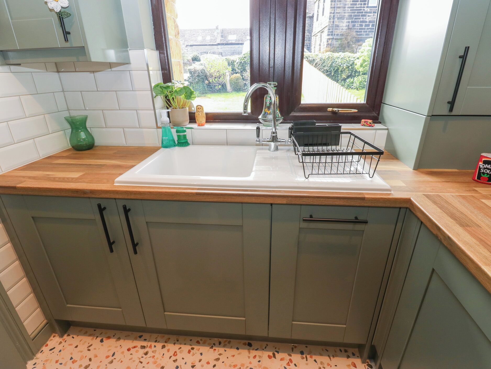 A kitchen with a white sink, wooden countertop, and grey cabinets.