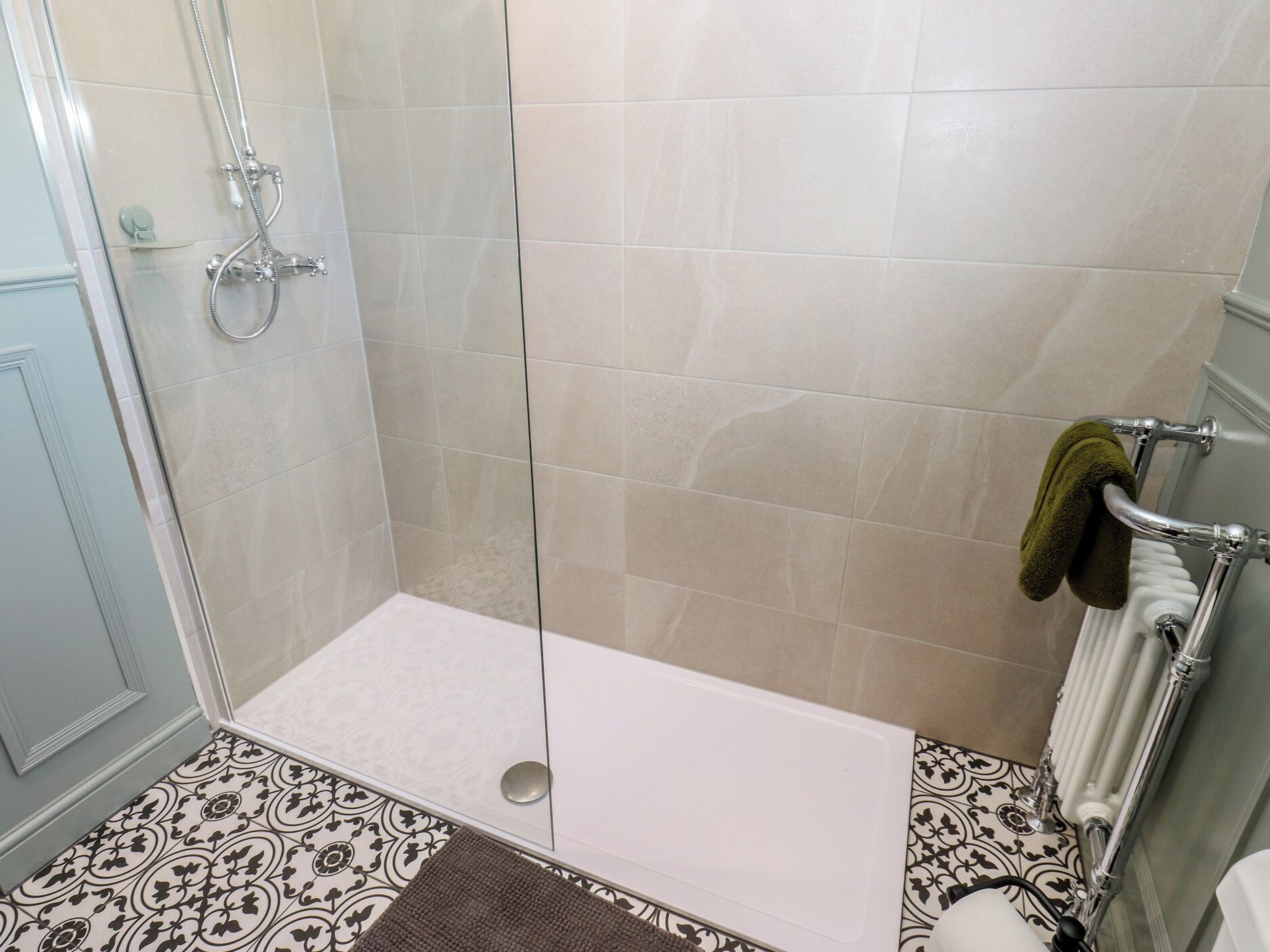 Una ducha con puerta de vidrio, una bañera blanca y un perchero con una toalla.