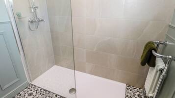 Una ducha con puerta de vidrio, una bañera blanca y un perchero con una toalla.
