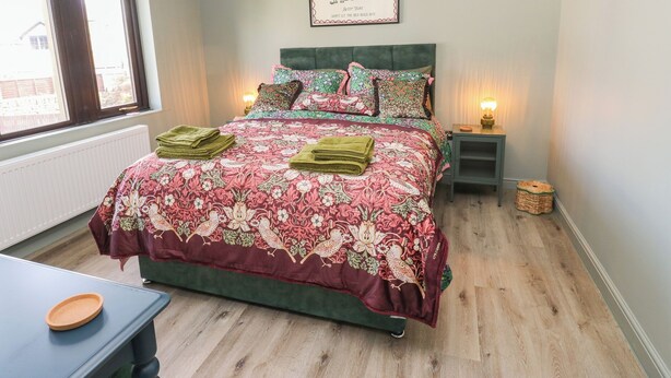 A bedroom with a bed, a bedside table, a lamp, a framed sign, and a window. - Underview (Holmfirth)