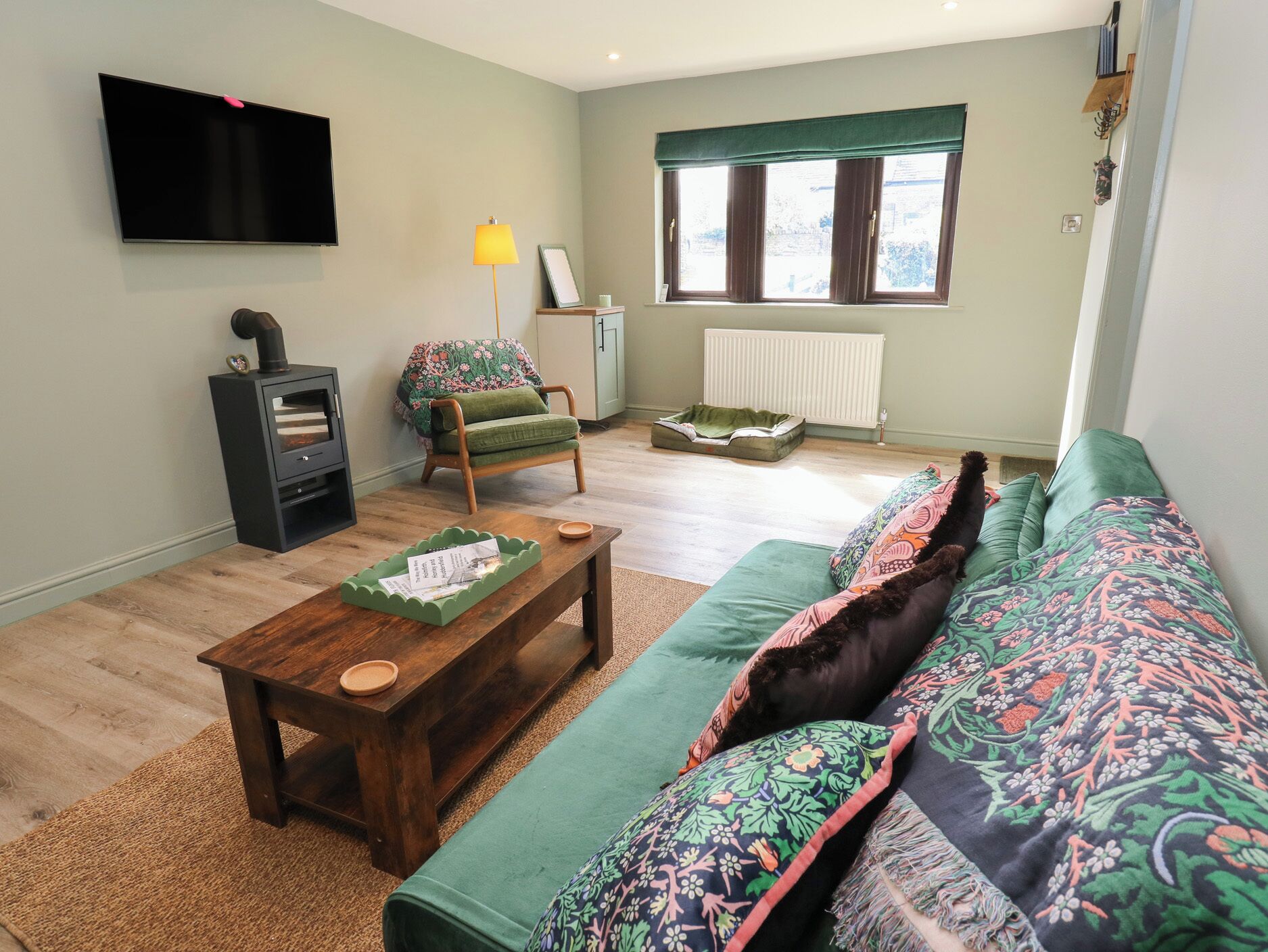 Una sala de estar con un sofá, una mesa de centro de madera, un sillón verde, una chimenea, un televisor y una ventana con cortinas.