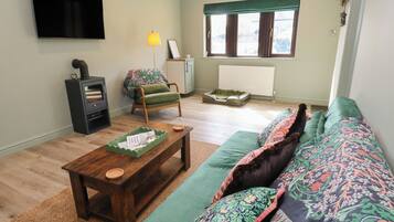 Una sala de estar con un sofá, una mesa de centro de madera, un sillón verde, una chimenea, un televisor y una ventana con cortinas.