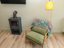 Una habitación con estufa de leña, sillón tapizado en verde y lámpara de pie amarilla.