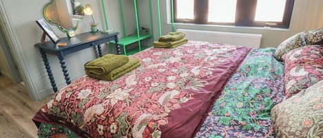 A bedroom with a bed, a desk, a mirror, and a window.