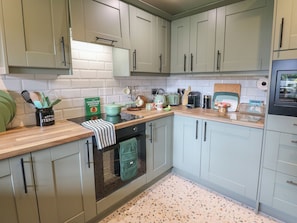A kitchen with light green cabinets, a countertop with various appliances, and a backsplash. - Underview (Holmfirth)