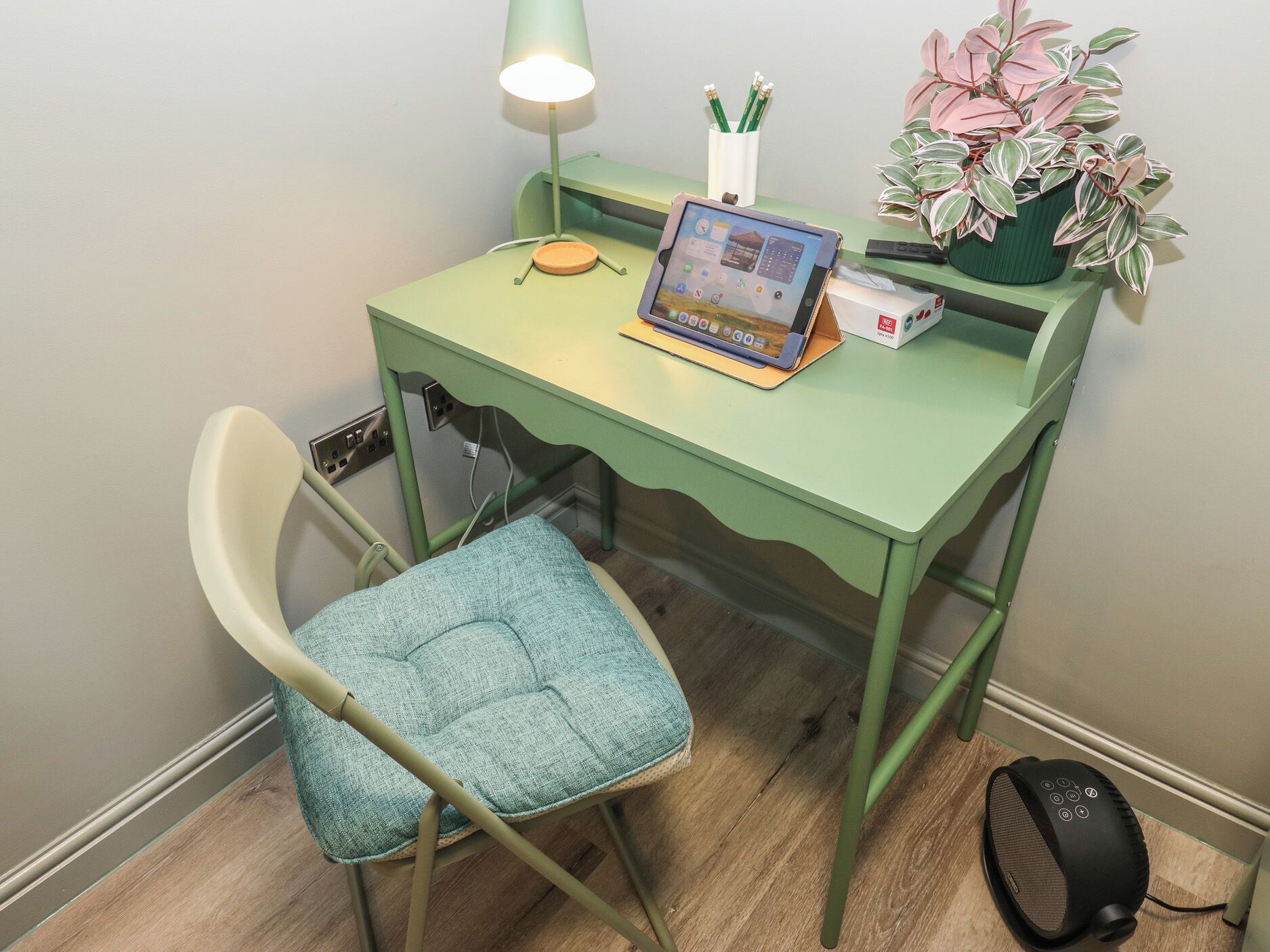 A green desk with a laptop, a lamp, a plant, and a speaker.