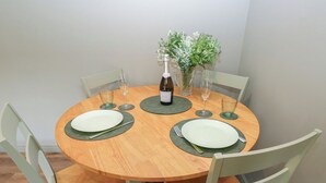 A round wooden dining table with four chairs, a bottle of wine, and a vase with flowers. - Underview (Holmfirth)