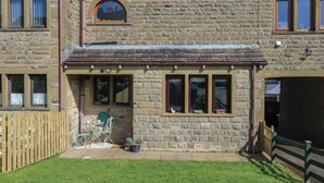 A stone building with a small front porch, a window with a view, and a number '6' on the wall. - Underview (Holmfirth)