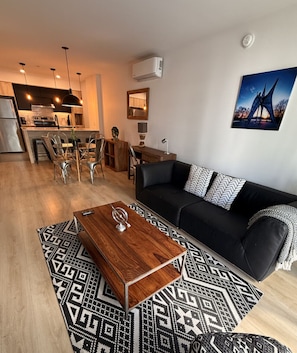 Ein modernes Wohnzimmer mit einer schwarzen Couch, einem gemusterten Teppich und einem Holztisch.