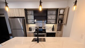 Una cocina moderna con una isla central, taburetes de bar, un refrigerador e iluminación colgante.