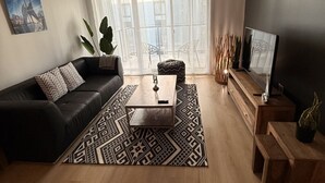 Una sala de estar moderna con un sofá de cuero negro, una mesa de centro de madera y un televisor sobre un mueble de madera.