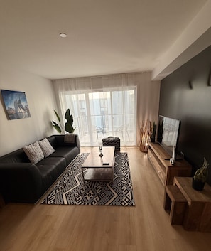 A modern living room with a black leather sofa, a wooden coffee table, and a TV on a wooden stand.