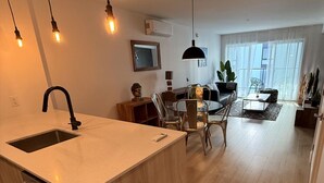 Una cocina moderna con una isla central, comedor con sillas, un sofá y un ventanal grande.