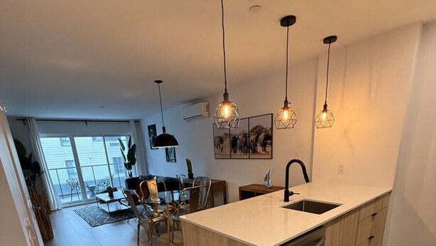 A modern kitchen with a central island, pendant lights, and a dining area with chairs and a table.