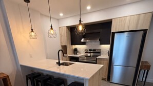 A modern kitchen with a central island, stainless steel appliances, pendant lighting, and a wooden bar stool area.