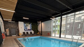 An indoor swimming pool with clear water, surrounded by tiled flooring and large windows.