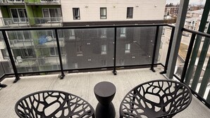 A balcony with two black chairs and a small table, overlooking a cityscape with modern buildings.