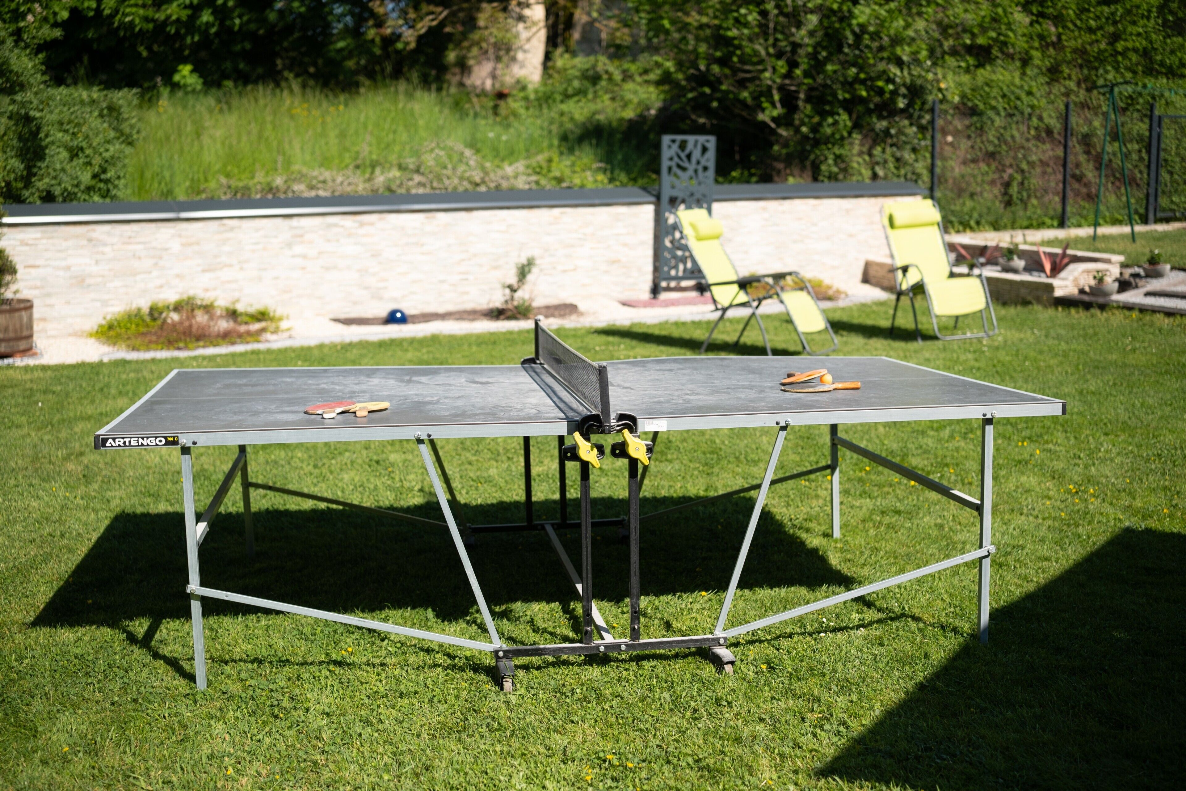 Une table de ping-pong avec un filet, installée dans un espace extérieur recouvert d’herbe.