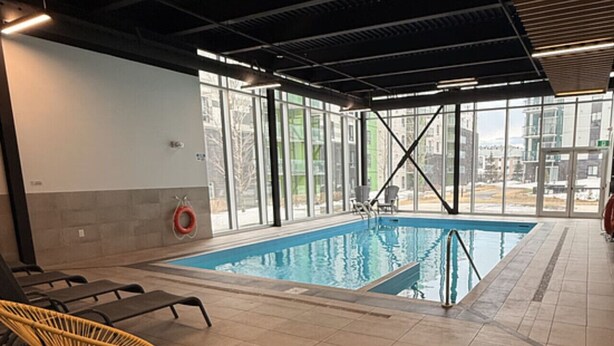 Ein Innenpool mit klaren Glaswänden, gefliestem Boden und einer Decke mit sichtbaren Balken und Beleuchtung.