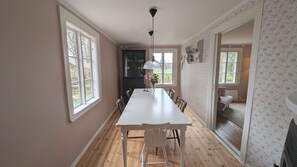 A dining room with a long table, chairs, a vase with flowers, and a kitchen in the background. - Idyllic and family friendly cottage in Småland | SE06095 (Ryssby)
