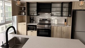 A modern kitchen with a central island, stainless steel appliances, and pendant lighting. - Modern 1BD Suite at Le Prisme w/ Private Balcony, Pool, Gym & Yoga Studio (Québec)