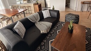 A modern living room with a black leather sofa, a wooden coffee table, and a patterned rug. - Modern 1BD Suite at Le Prisme w/ Private Balcony, Pool, Gym & Yoga Studio (Québec)