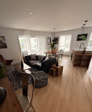 Ein modernes Wohnzimmer mit Sofa, Esstisch, Stühlen und einer Küchenzeile mit Spüle und Arbeitsfläche.