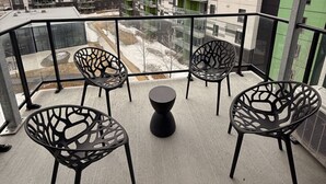 A balcony with four chairs and a central table, overlooking a residential area with multi-story buildings. - Modern 1BD Suite at Le Prisme w/ Private Balcony, Pool, Gym & Yoga Studio (Québec)