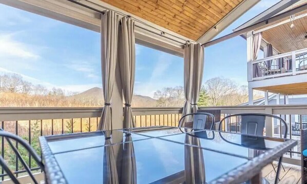 Ein Glastisch mit Stühlen auf einem Balkon mit Blick auf Berge und Bäume.