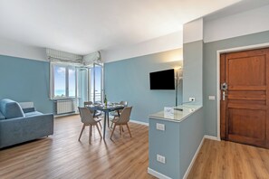 A modern living room with a sofa, dining table, chairs, a TV, and a wooden door. - Kenyon Charm - Total Sea View (Alassio)