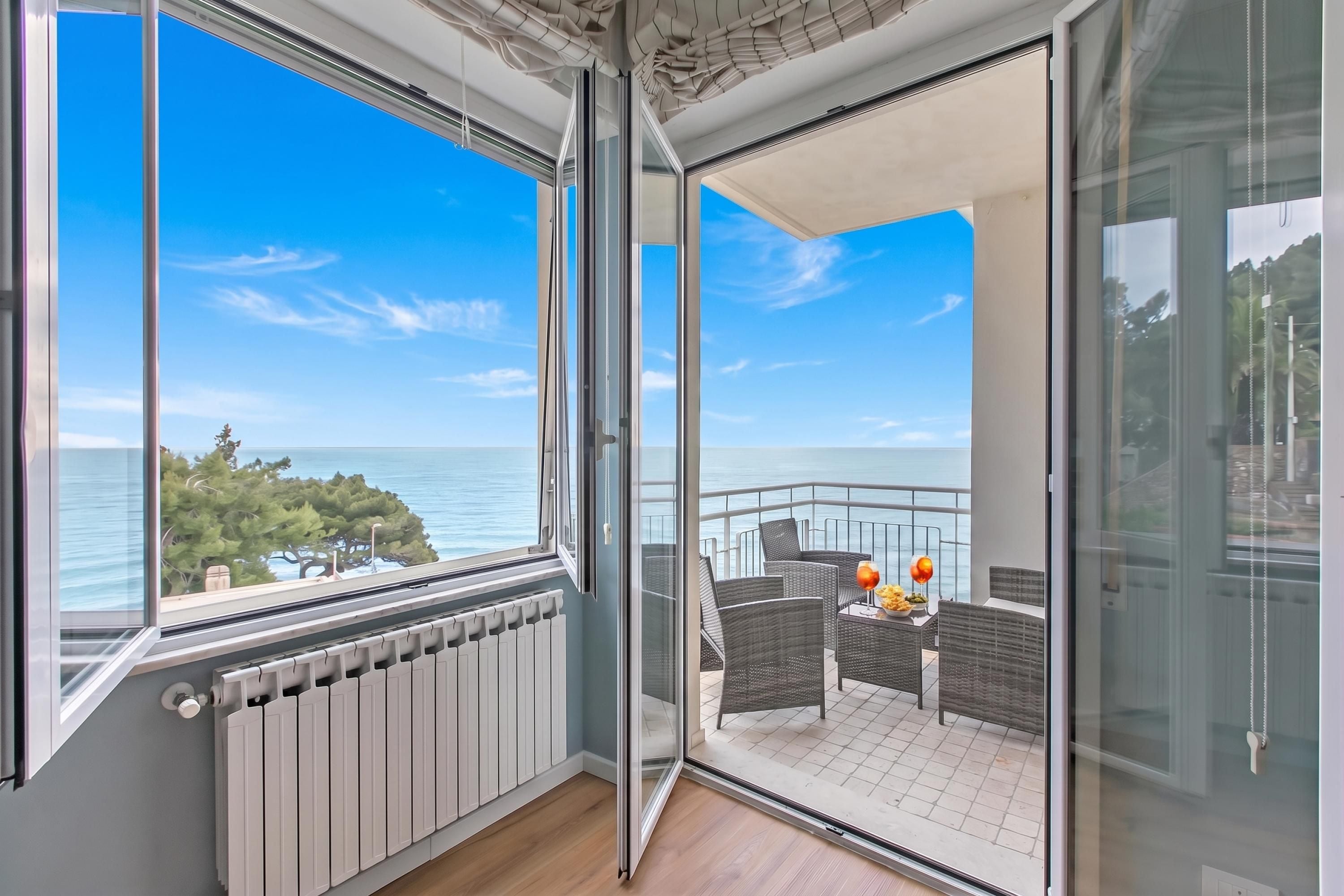 Un balcon donnant sur la mer, aménagé avec des fauteuils et une table en osier, et un radiateur blanc fixé au mur.