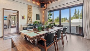 Un coin repas avec une table et des chaises en bois, une grande fenêtre donnant sur des arbres et un bâtiment, et un mur orné d’une enseigne publicitaire pour du café.