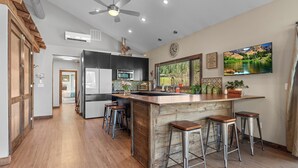 Une cuisine moderne dotée d’un îlot central, de tabourets de bar, d’un ventilateur de plafond et d’une grande fenêtre offrant une belle vue.