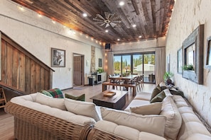 A spacious living area with a large sofa, dining table, and chairs, wooden ceiling, and large windows. - New Listing! Large Barn Home | Rustic-Chic Retreat | Hot Tub | Sauna (Coeur d'Alene)