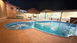 Ein Schwimmbad mit Whirlpool, Liegestühlen und einem Strohdachschirm.